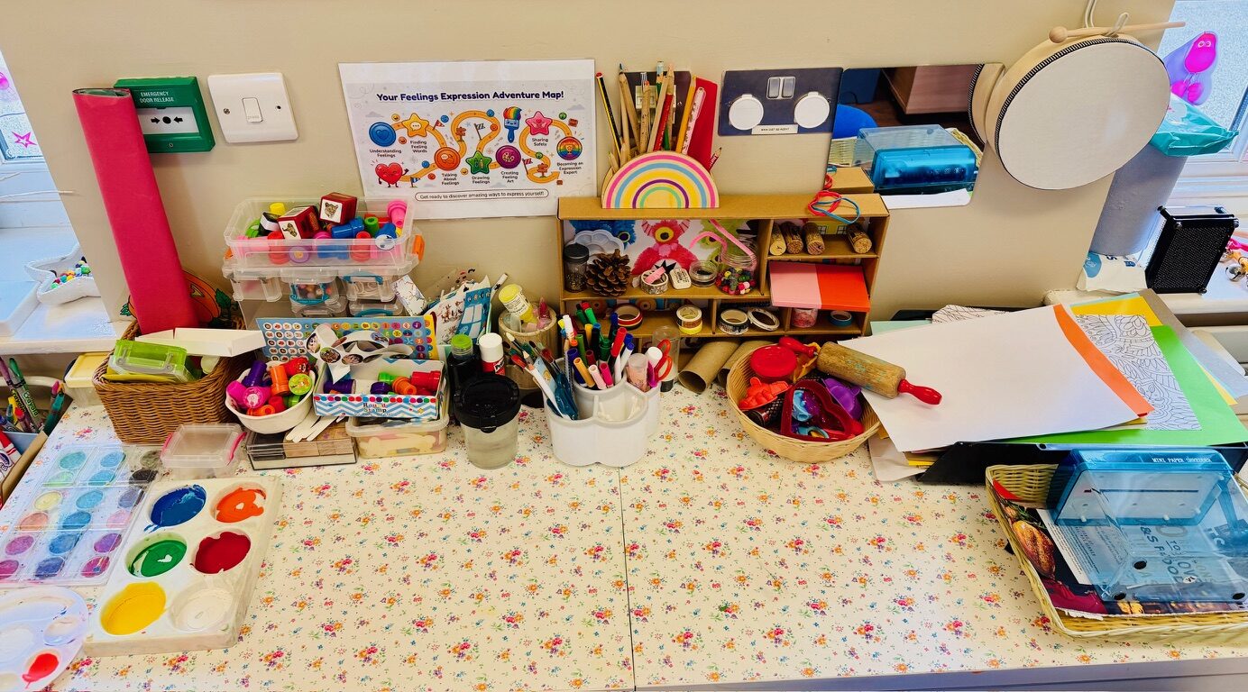 An art and craft table with paints, pens and a feelings expression poster