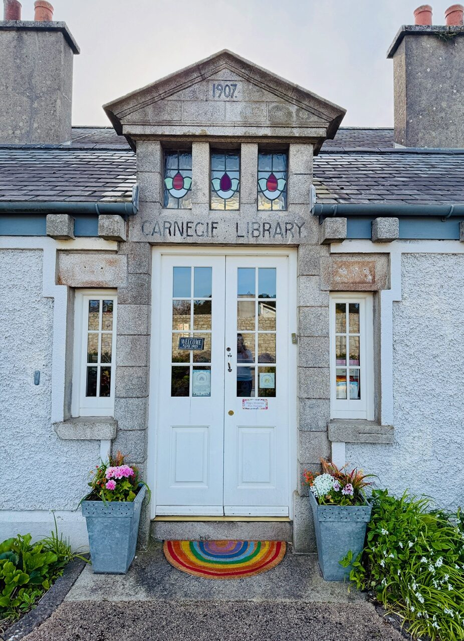 A welcoming front door with flower pots either side and a rainbow doormat on the step