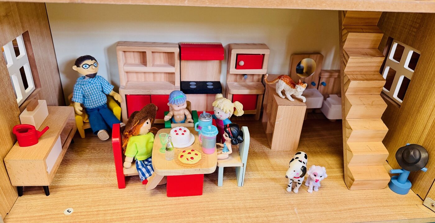 A furnished dolls' house kitchen with a family of small wooden figures around a table