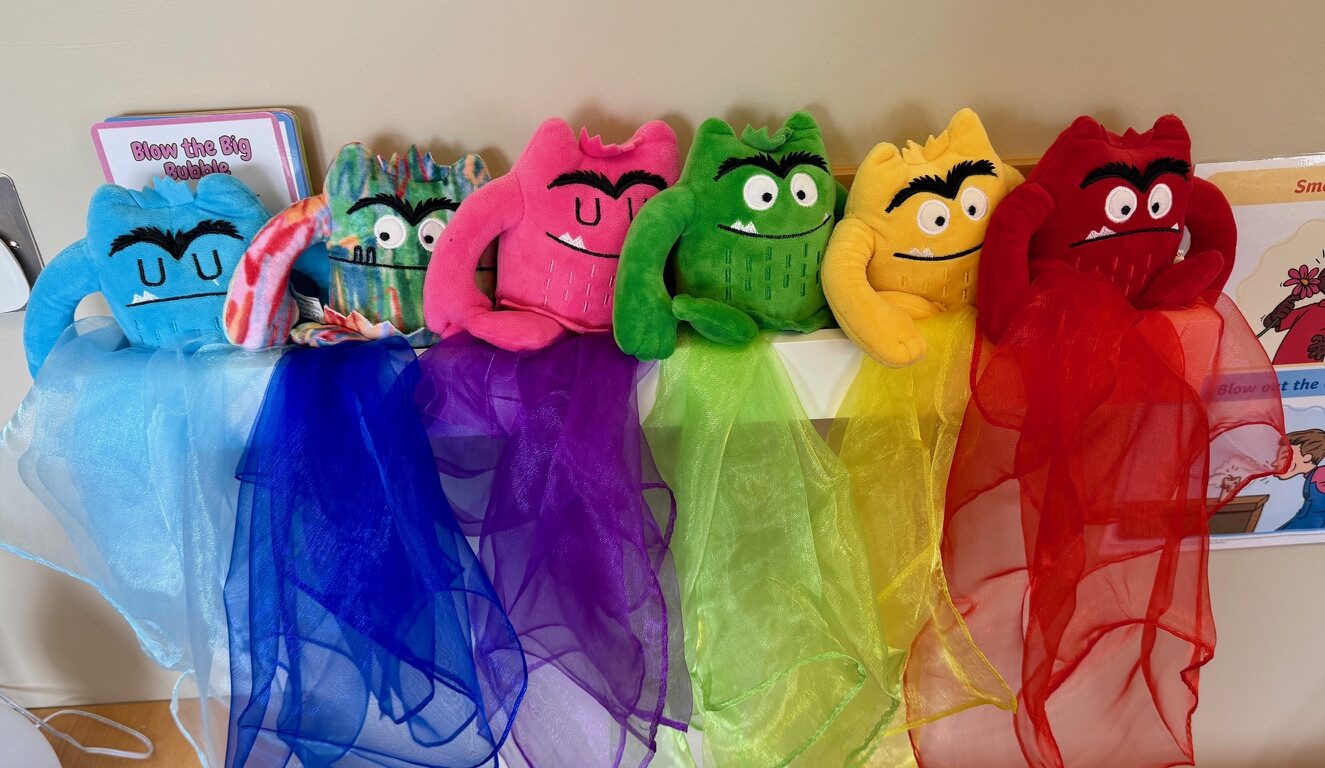 Six soft feelings monsters in rainbow colours, each with a matching coloured scarf