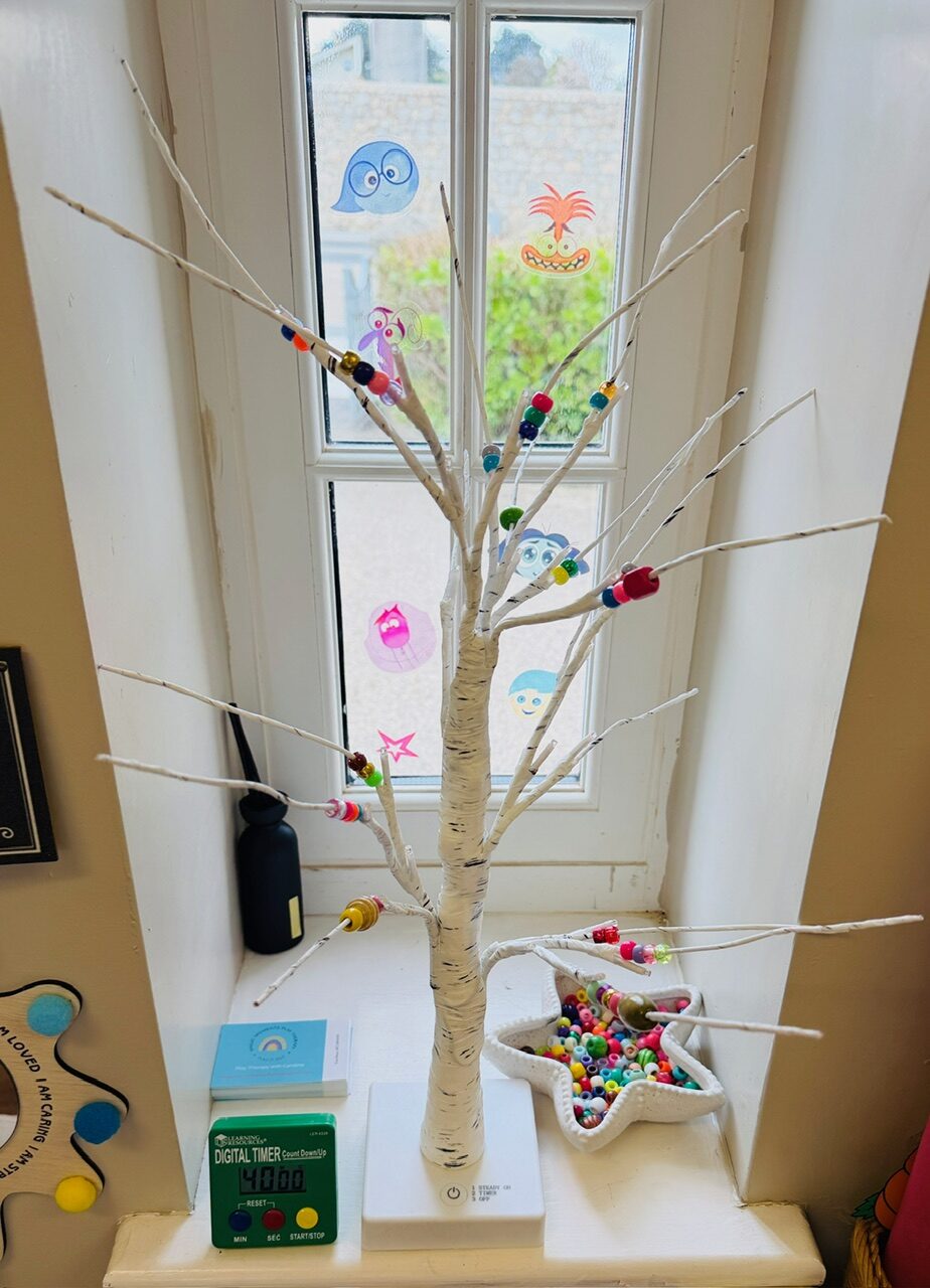 A small white twig tree decorated with coloured beads beside a star-shaped bowl of beads